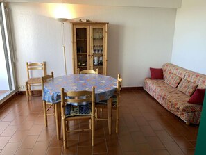 A dining area with a round table, chairs, a cabinet with glass doors, and a sofa. - Apartment 2BR+2 Cabins, Terrace, Parking, 8 Pers - Port Camargue (Port Camargue)
