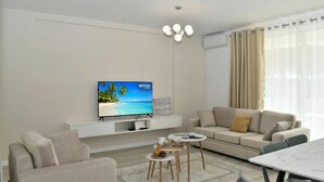 Una sala de estar moderna con un televisor de pantalla plana, un sofá, una mesa de centro y una mesa de comedor.