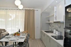 A modern kitchen with white cabinets, a black countertop, and a built-in oven. - White Moon Apartments (Ishëm)
