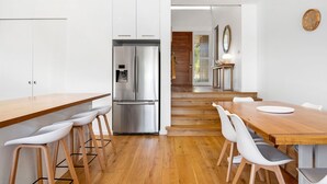 A modern kitchen with a stainless steel refrigerator, wooden bar stools, and a wooden dining table with chairs.