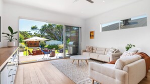 A spacious living room with a large sliding glass door leading to a backyard, a ceiling fan, and a view of the sky.