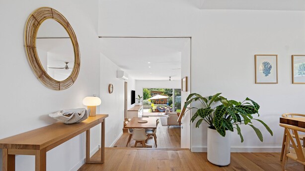 A modern interior with a wooden floor, a round mirror, a dining area with a table and chairs, and a potted plant.