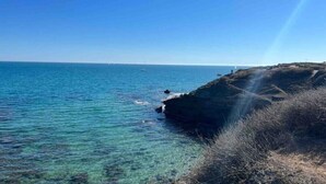 Eine Küstenlandschaft mit klarem, blauem Wasser, felsigen Klippen und einem Leuchtturm in der Ferne.
