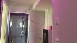 Ein Badezimmer mit einer gläsernen Duschkabine, weißen Marmorwänden und einer Wand in Rosé.