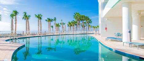 A swimming pool with a clear blue water surface, surrounded by palm trees and a white building with a curved roof.