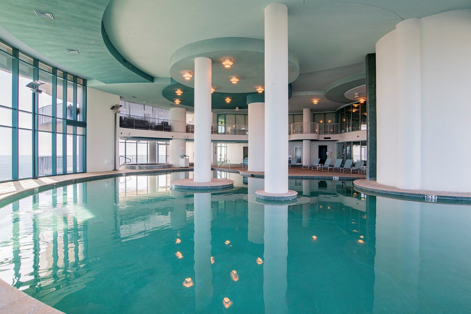 An indoor swimming pool with multiple levels and a view of the ocean through large windows.