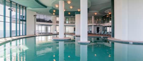 An indoor swimming pool with multiple levels and a view of the ocean through large windows.