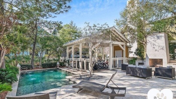 A pool area with lounge chairs, a covered seating area, and a stone fireplace. - WaterColor Escape |Bring the Whole Family—Pups Included! Sleeps 8 (Santa Rosa Beach)