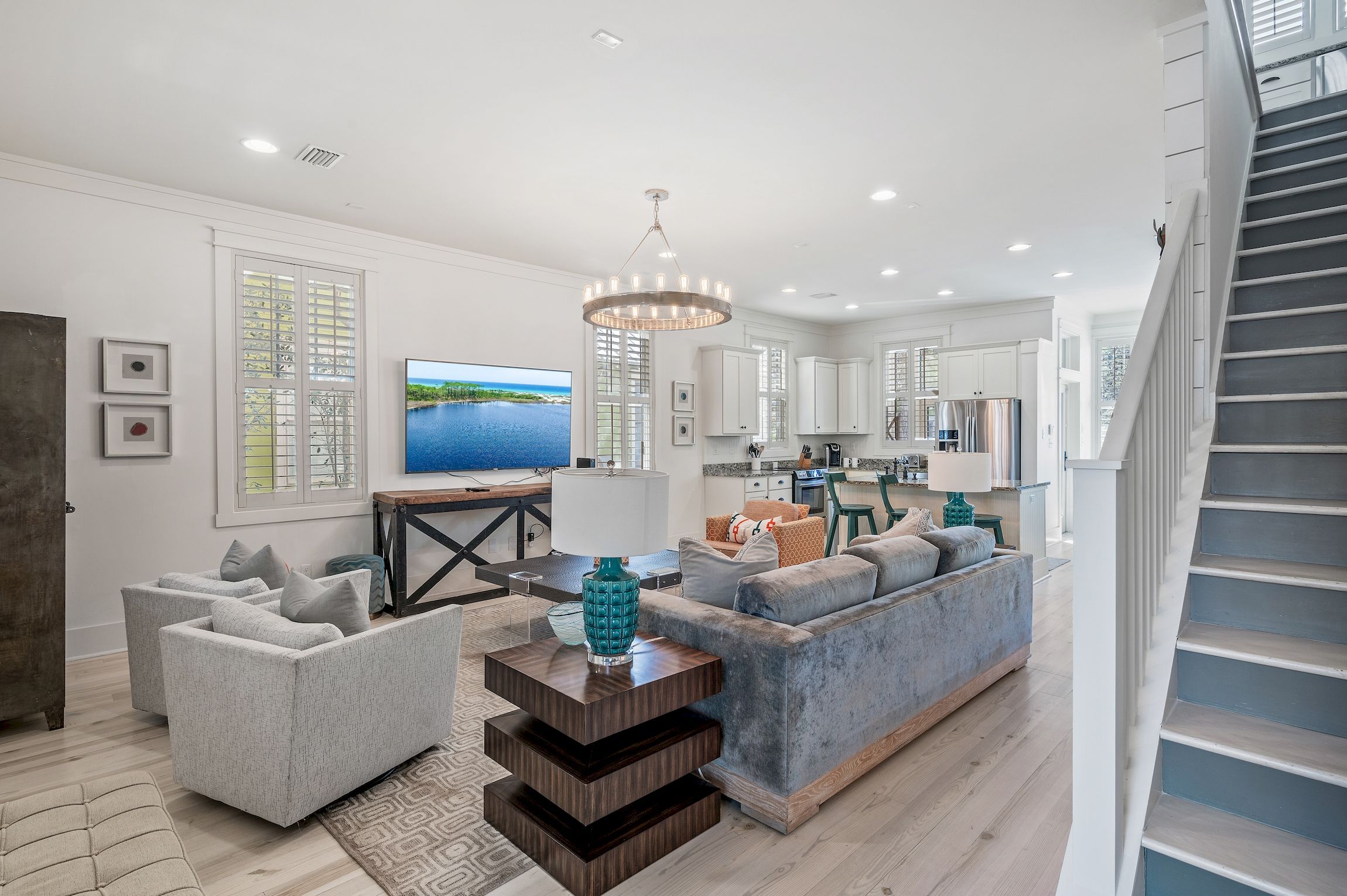 A spacious living room with a grey sofa, a blue accent piece, and a flat-screen TV.