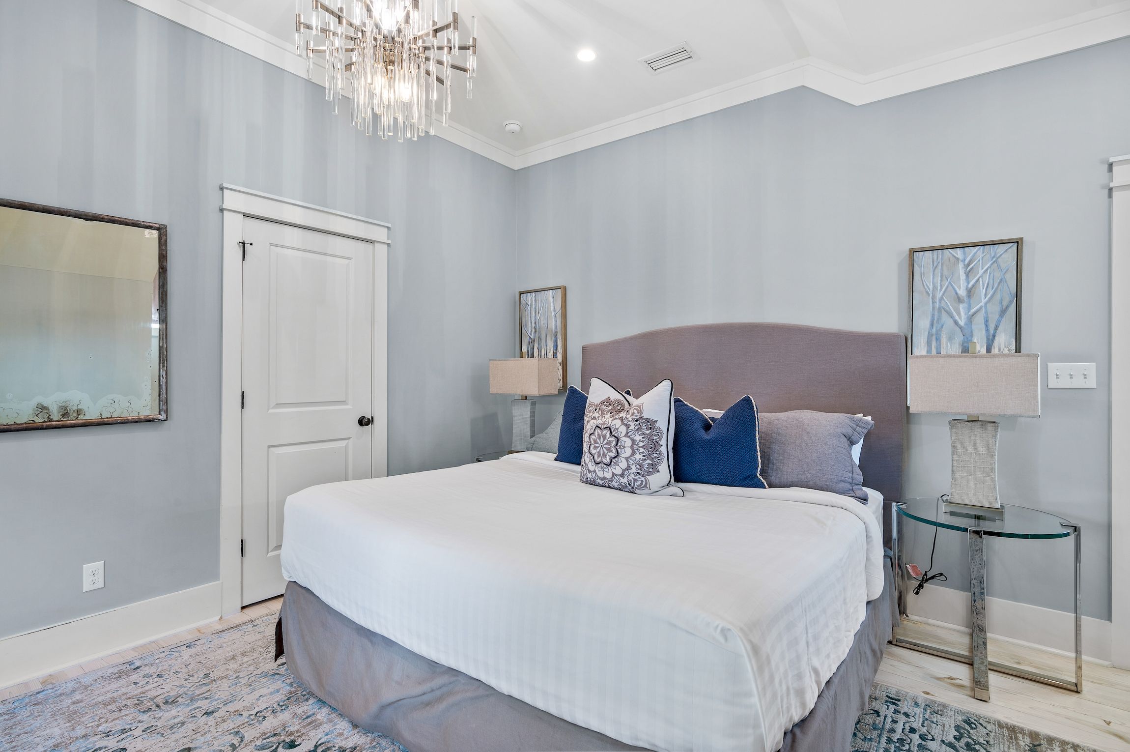 A bedroom with a large bed, two bedside tables, a chandelier, and a framed picture on the wall.