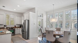 A modern kitchen with white cabinetry, stainless steel appliances, and a dining area with a chandelier. - WaterColor Escape |Bring the Whole Family—Pups Included! Sleeps 8 (Santa Rosa Beach)