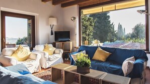 Ein Wohnzimmer mit zwei Sofas, einem Fernseher und einem großen Fenster mit Blick auf Bäume und ein Dach.