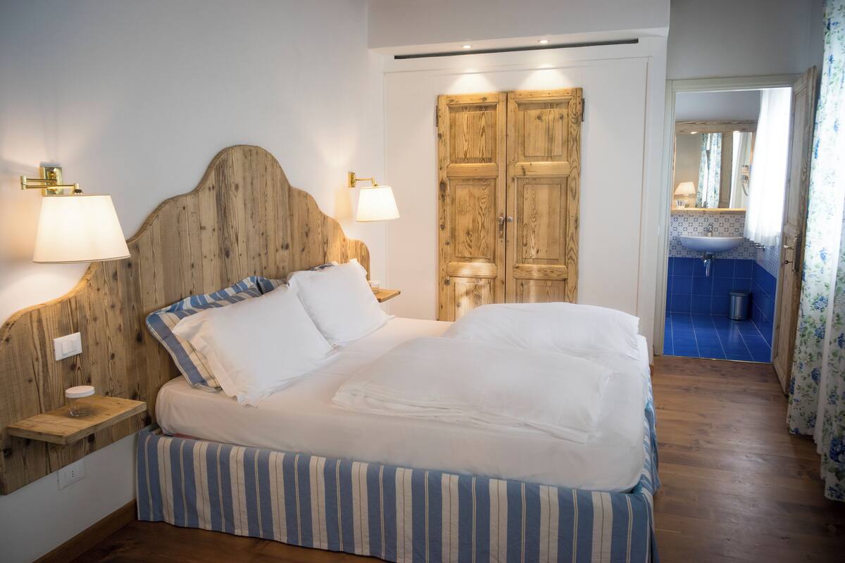 Un lit bien fait, avec une literie à rayures, une tête de lit en bois, des lampes de chevet et une armoire en bois dotée d’un miroir.