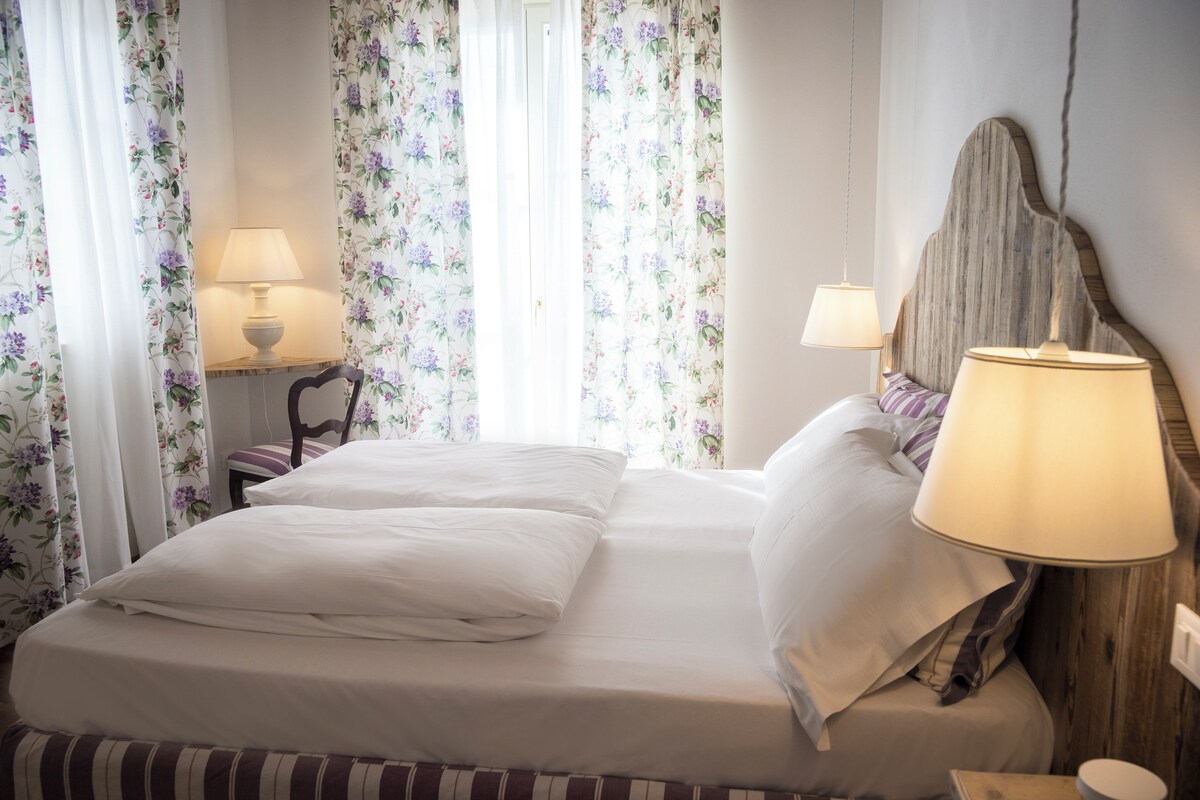 Een netjes opgemaakt bed met witte lakens, een houten hoofdbord en twee bedlampen.