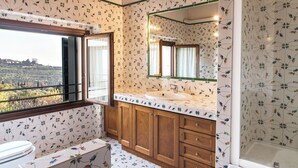 Ein Badezimmer mit großem Fenster, Holzschränken, einem Waschbecken und einem Spiegel.