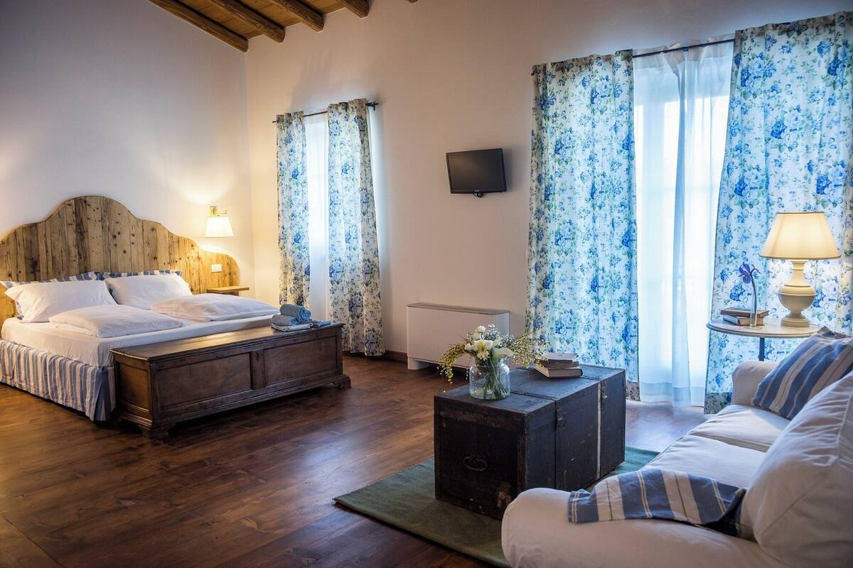 Une chambre à coucher avec un lit en bois, une table de chevet avec une lampe, une petite table sur laquelle est posé un vase de fleurs et un canapé.