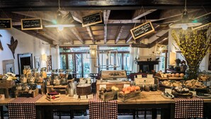 Ein rustikales Café-Interieur mit Holztischen, karierten Tischdecken, hängenden Lampen und verschiedenen Speisen, die auf den Tischen präsentiert werden.