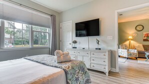 A bedroom with a bed, a dresser, a TV, and a view of the outside.