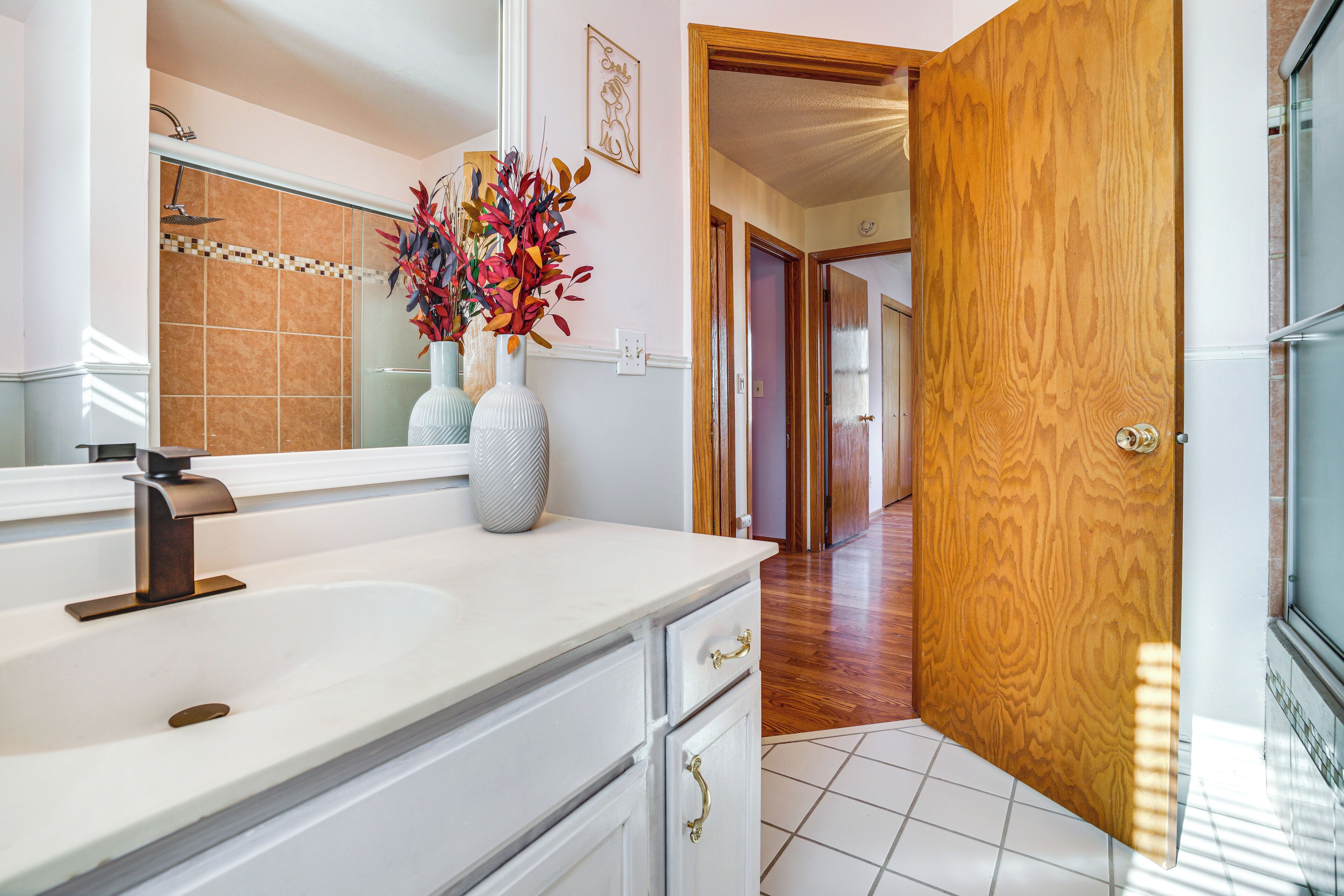 Un baño con lavamanos blanco, un espejo y una puerta de madera que da a otra habitación.