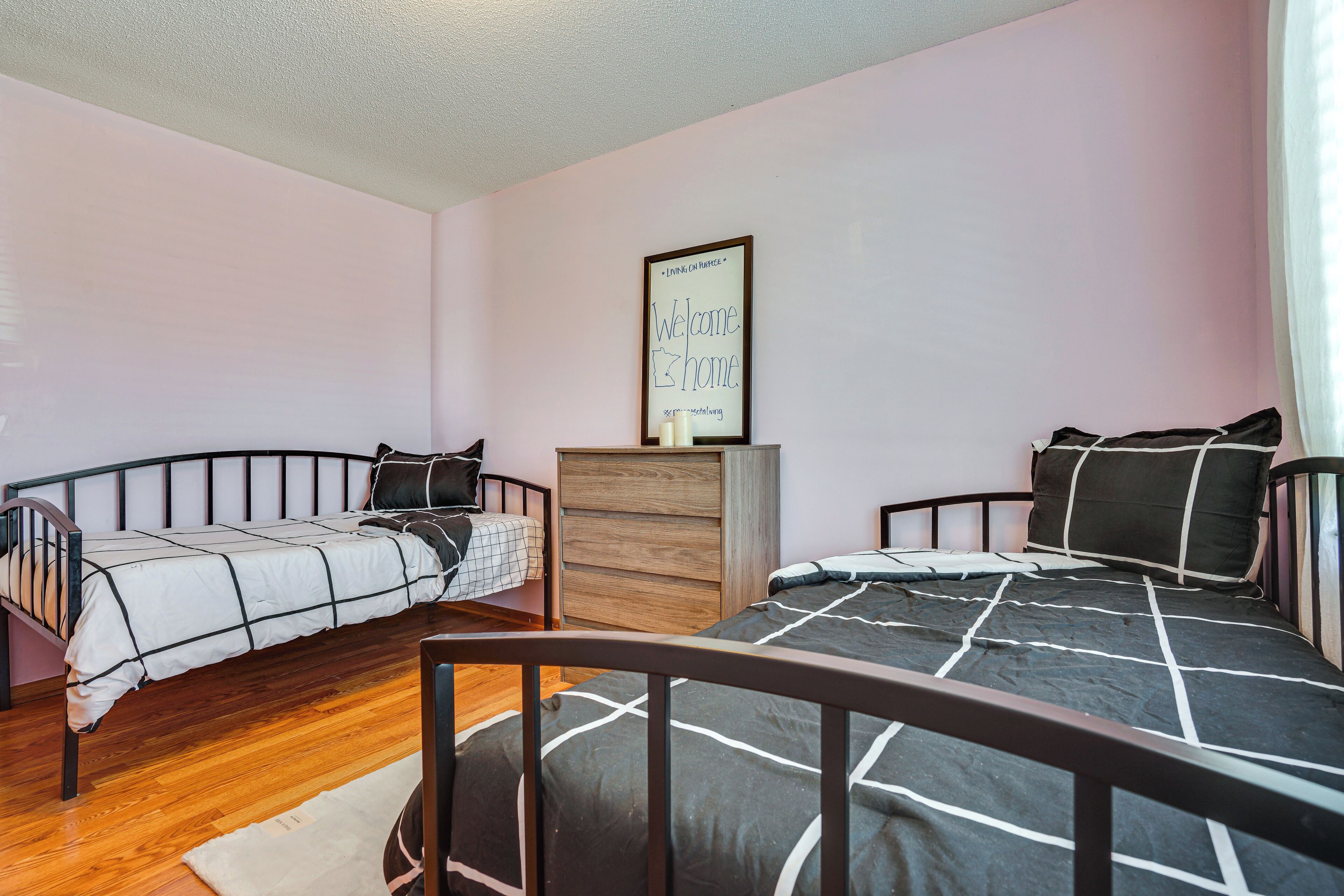 A bedroom with two beds, a wooden dresser, and a framed sign on the wall.