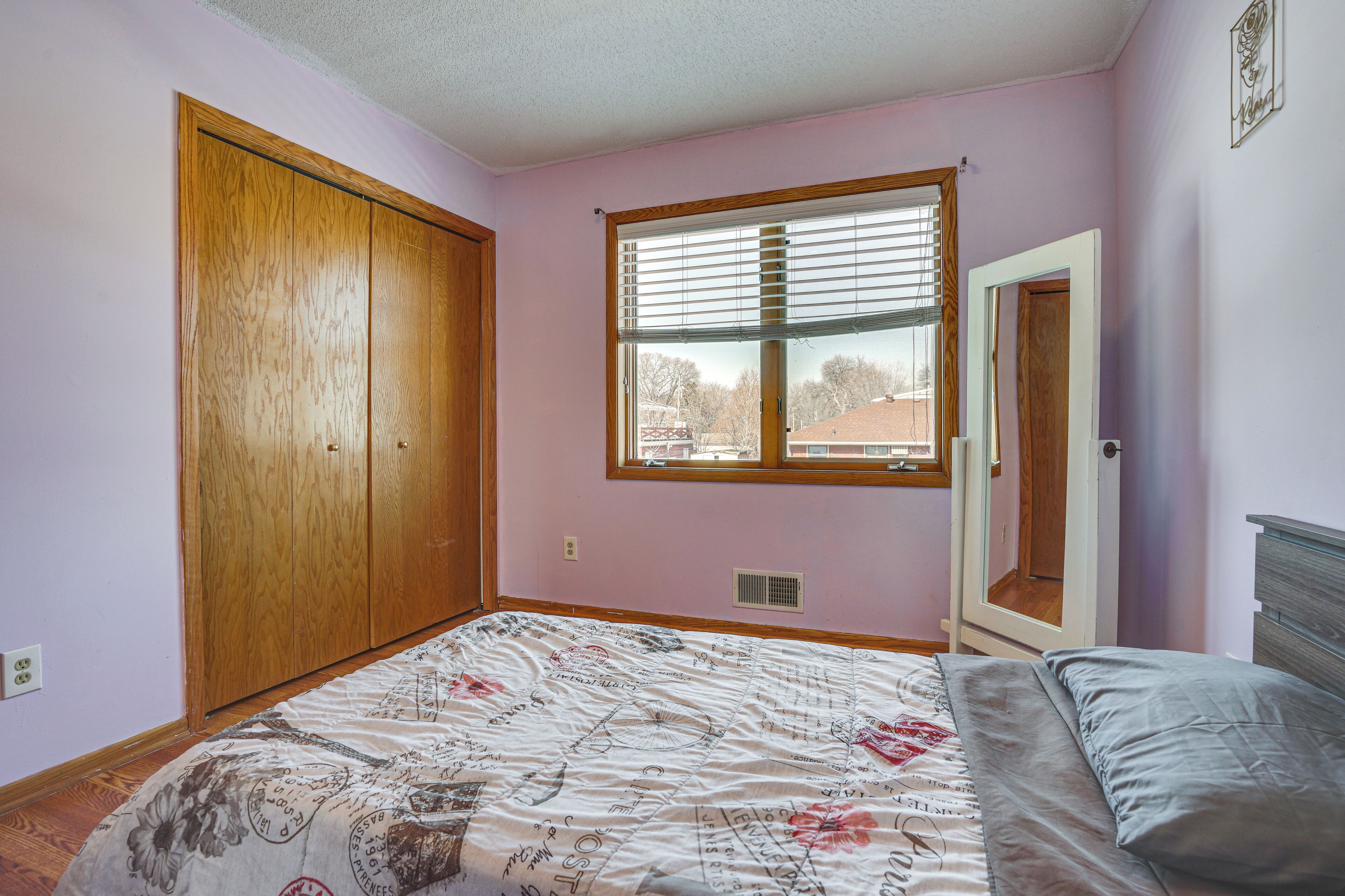A bedroom with a bed, a window with blinds, a wooden wardrobe, and a door.