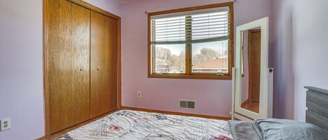 A bedroom with a bed, a window with blinds, a wooden wardrobe, and a door.