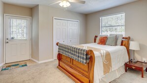 A bedroom with a wooden bed, a ceiling fan, a nightstand, a lamp, and a window with blinds. - Cozy Jacksonville Home ~ 12 Mi to Downtown! (Jacksonville)