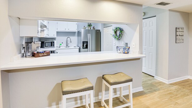 A modern kitchen with white cabinets, a stainless steel refrigerator, a microwave, and a coffee station. - Updated Tallahassee Townhome: 3 Mi to Downtown! (Tallahassee)
