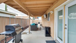 Ein überdachter Patio-Bereich mit Grill, Sitzgelegenheit und einer Tür.