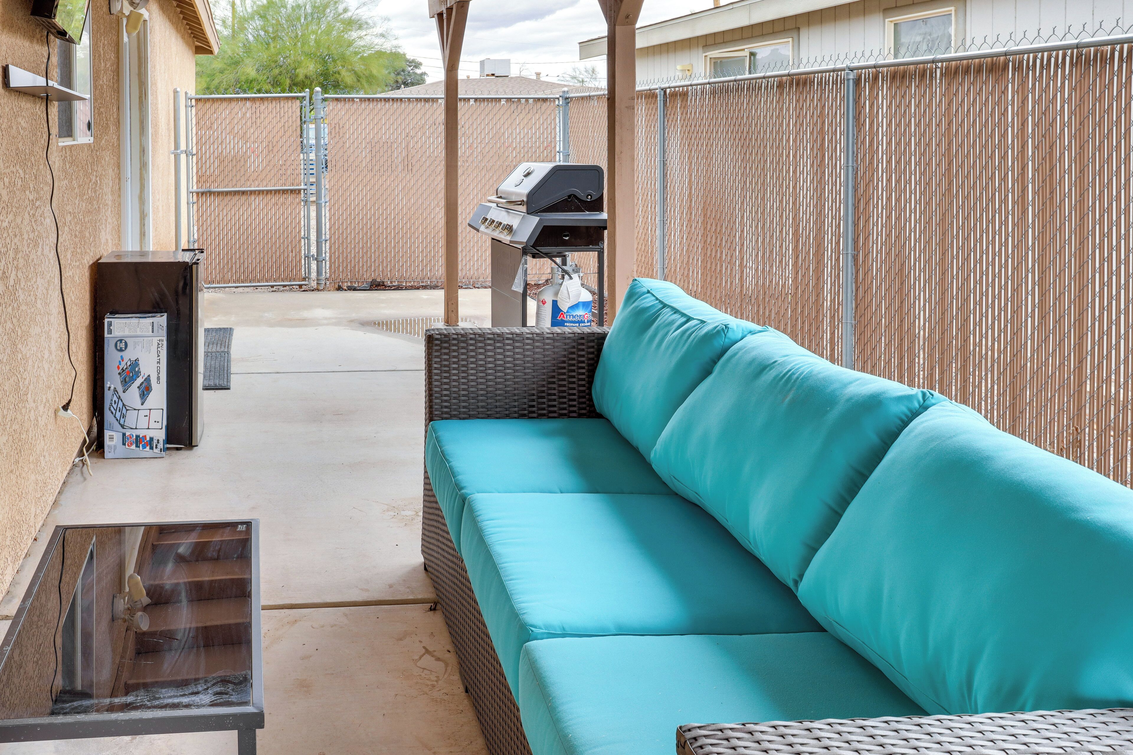 Une terrasse extérieure avec un canapé turquoise doté de coussins, un barbecue et une table en verre.