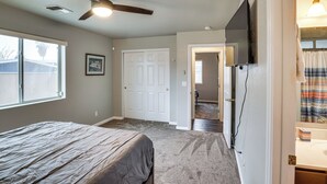 Ein Schlafzimmer mit einem Bett, einem Deckenventilator, einem an der Wand befestigten Fernseher und einer Tür zu einem weiteren Raum.
