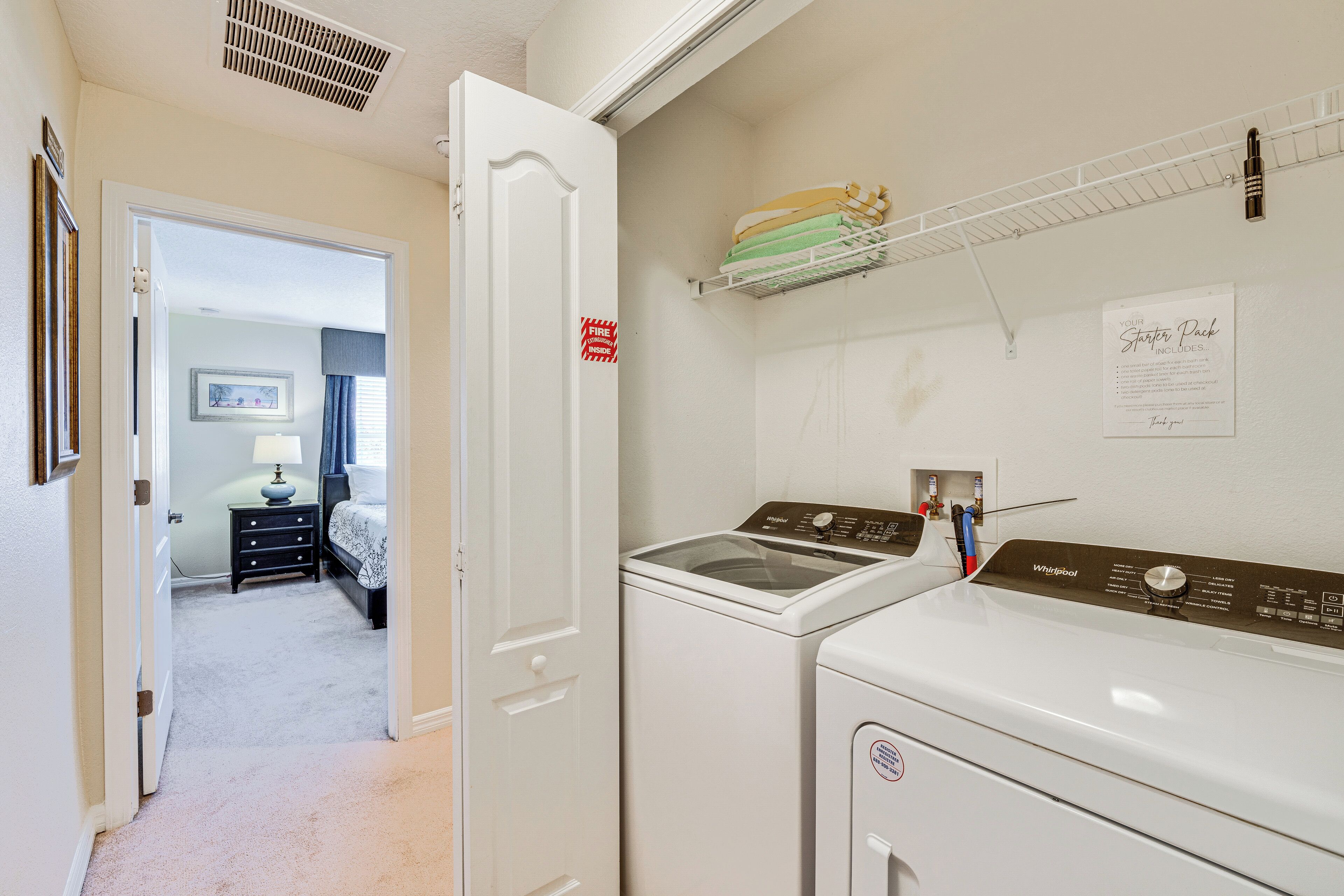 A laundry room with a washer and dryer, a shelf with folded clothes, and a fire exit sign.