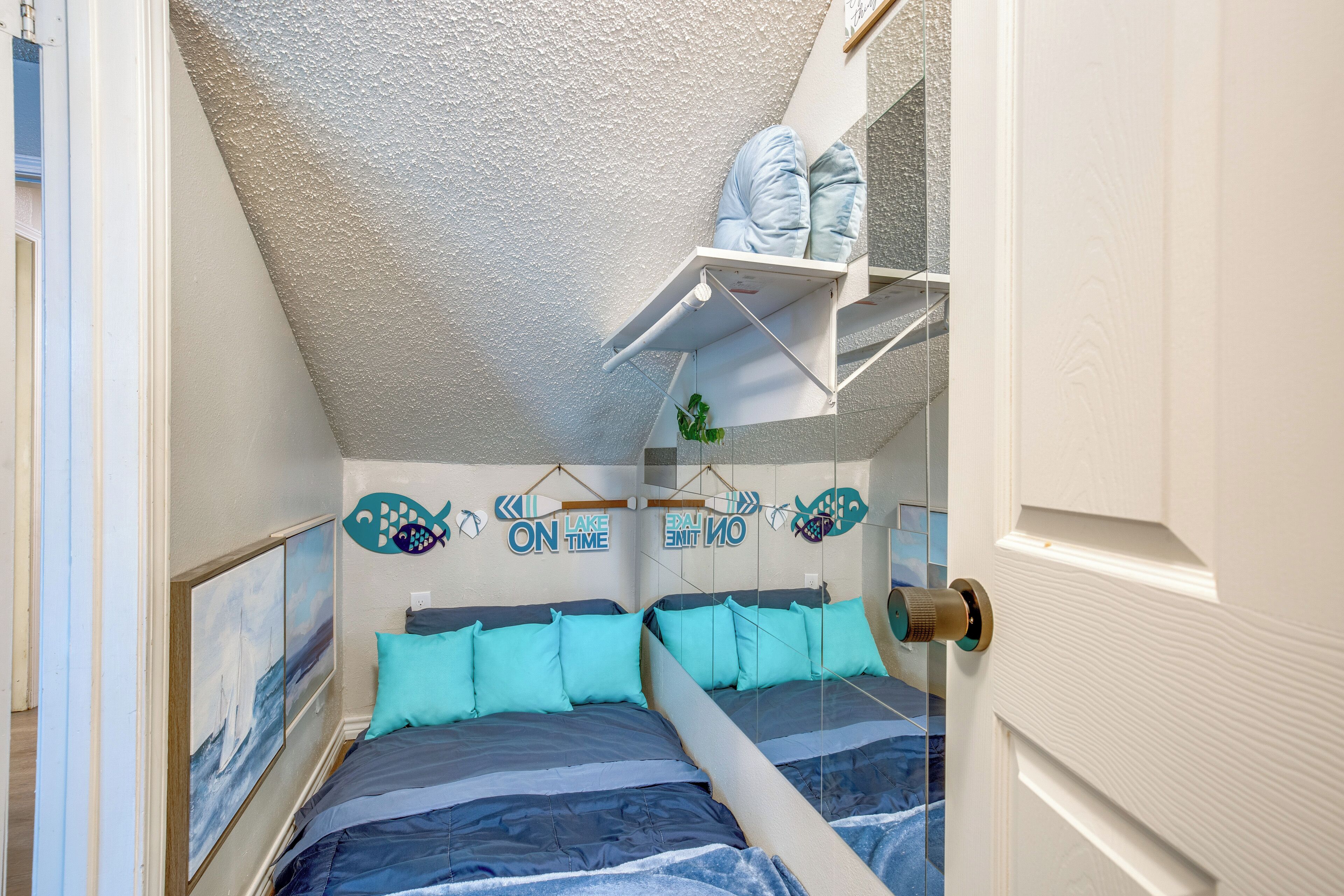 A bedroom with a bunk bed, a ceiling fan, a shelf with pillows, and a door with a brass handle.