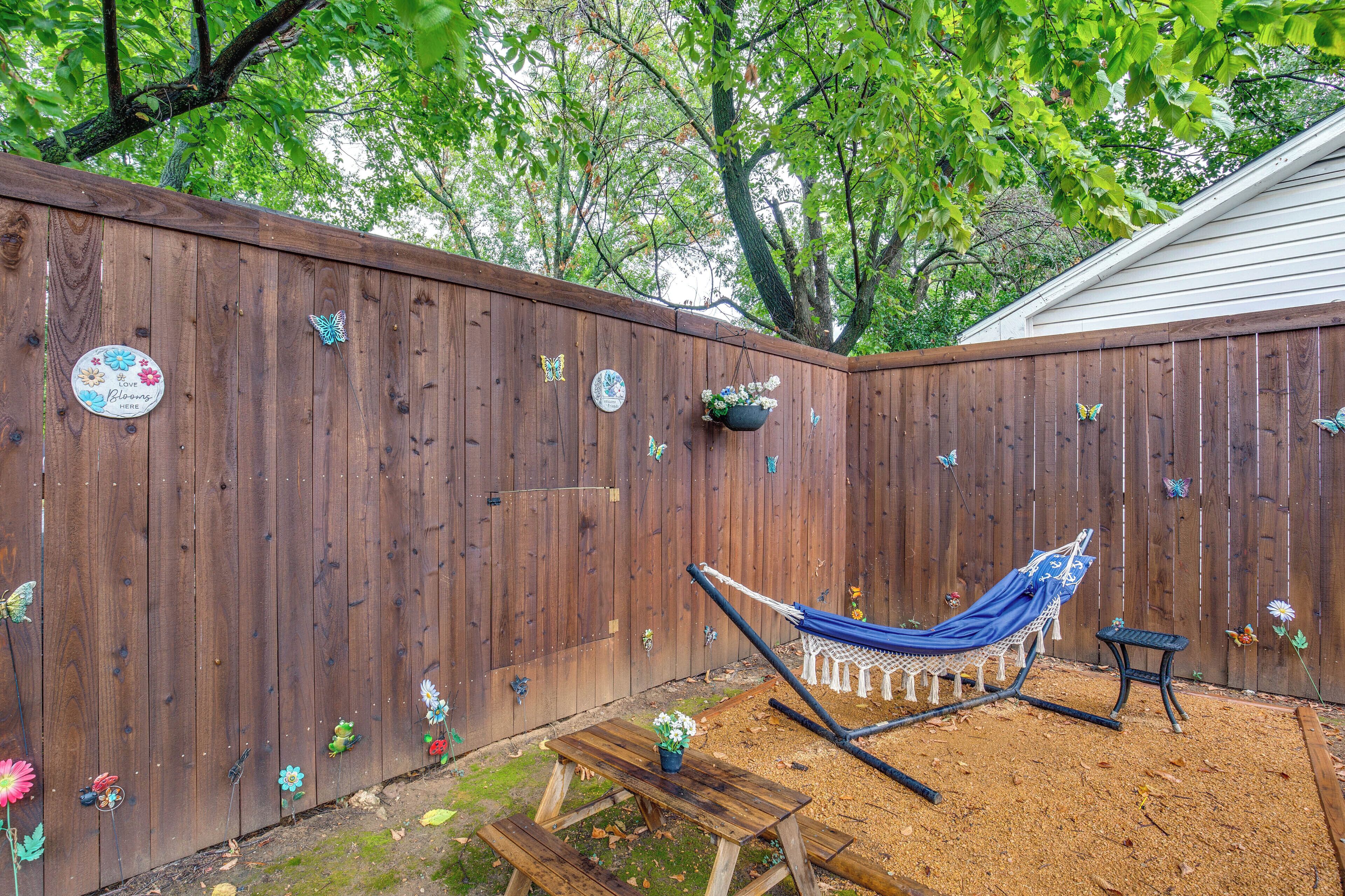 A wooden fence with butterfly decorations, a hammock, and a small table with a potted plant.