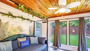 Un salon moderne avec un canapé, un ventilateur de plafond et une vue sur le jardin à travers de grandes fenêtres.