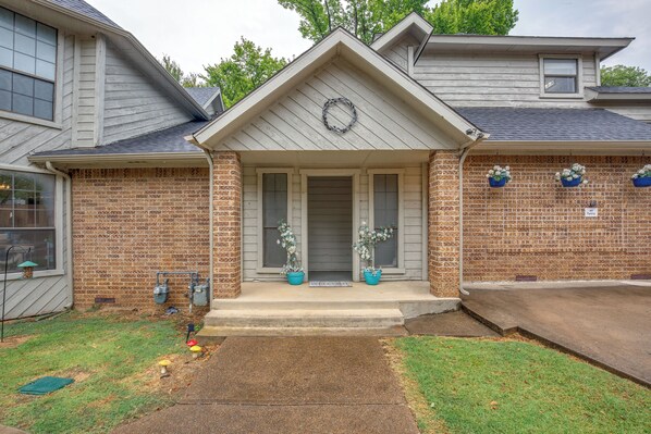 A two-story house with a brick facade, a front porch with a wreath, and two potted plants.