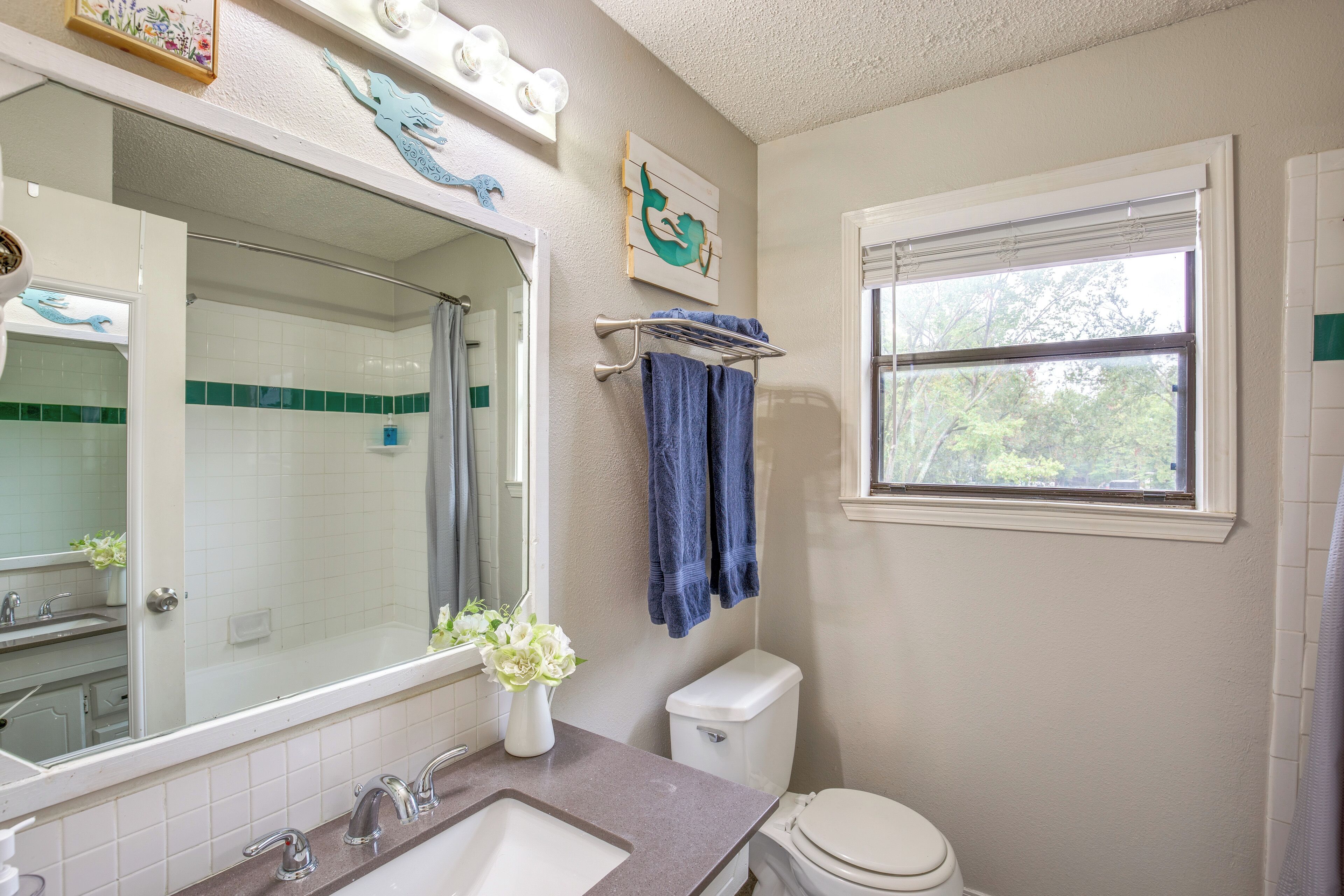 A bathroom with a large mirror, a sink, a toilet, and a window.