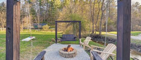 A wooden pergola with a fire pit in the center, surrounded by outdoor seating and a grassy area.