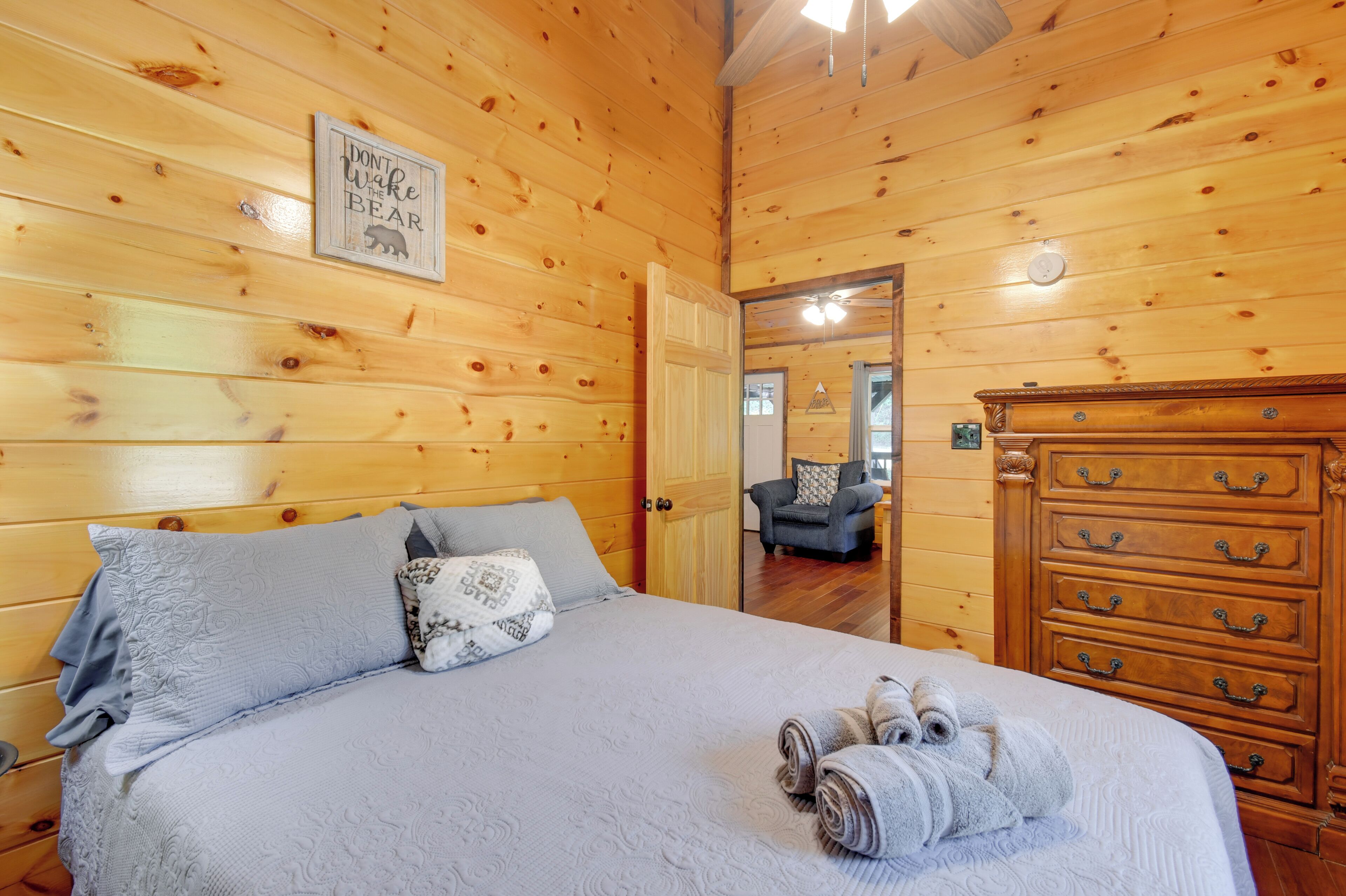 A wooden-paneled room with a bed, a dresser, and a framed sign on the wall.