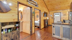 Interior de una cabaña de madera con una zona de cocina, una cama y una chimenea.