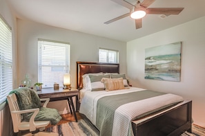 A bedroom with a bed, a desk, a chair, a ceiling fan, and a painting on the wall.