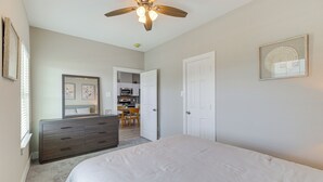 A bedroom with a bed, a dresser, a ceiling fan, and a door leading to a kitchen. - Easy Interstate Access: Quiet Houston Home! (Houston)