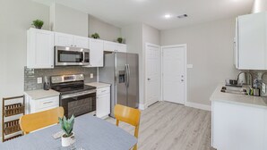 A modern kitchen with white cabinetry, stainless steel appliances, and a dining area with a table and chairs. - Easy Interstate Access: Quiet Houston Home! (Houston)
