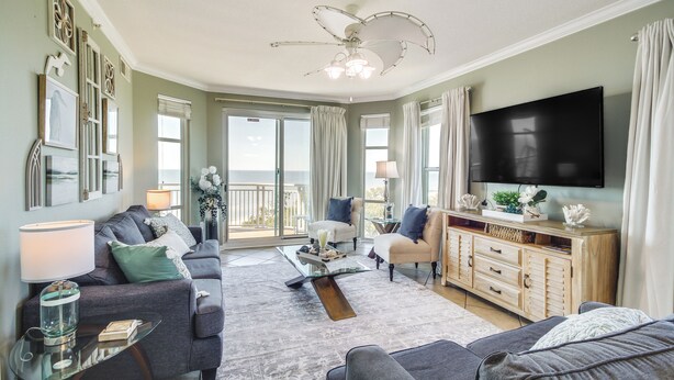 A spacious living room with a ceiling fan, a flat-screen TV, and a large window offering a view of the outdoors. - Gulfport Oceanfront Vacation Rental: Walk to Beach (Gulfport)