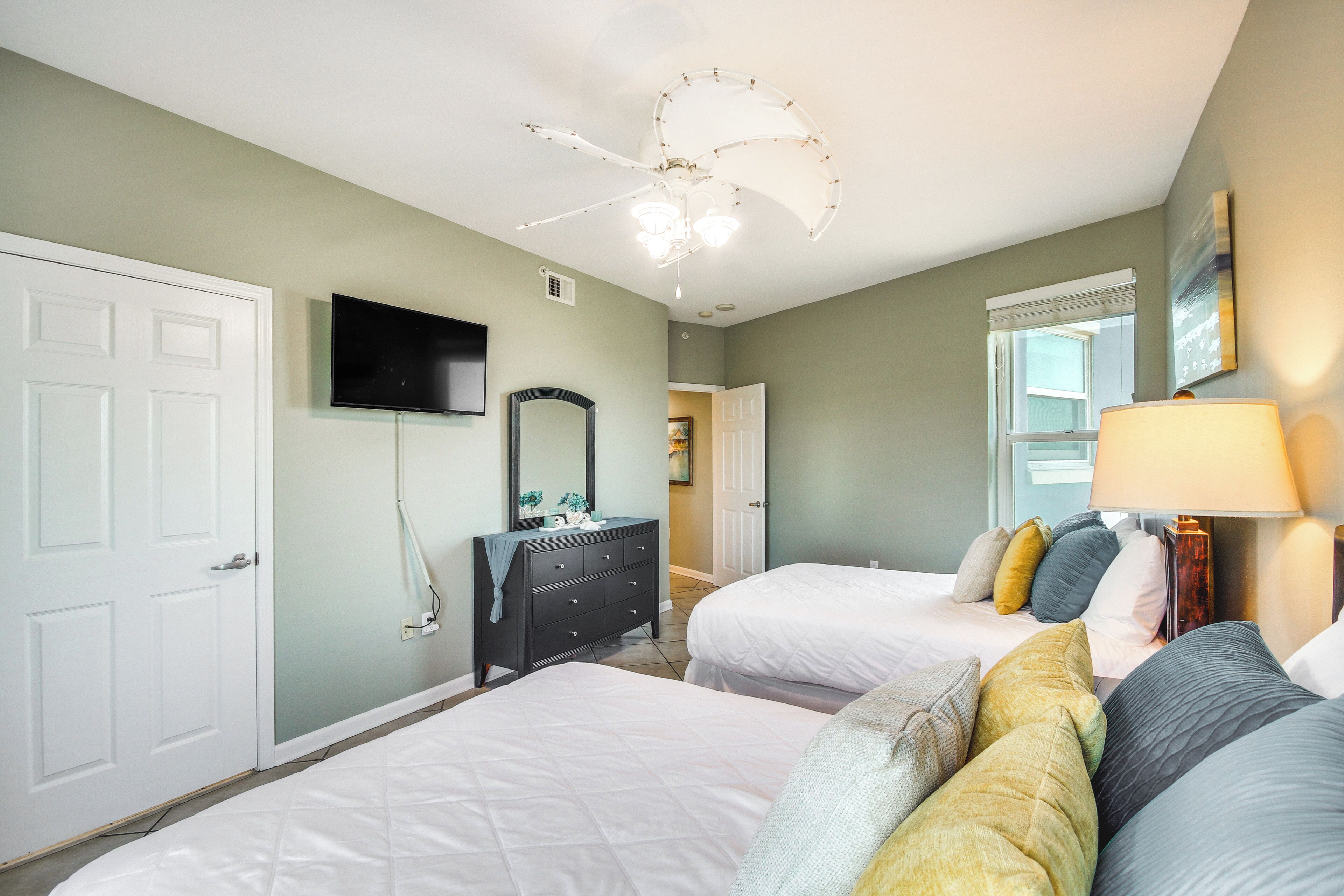 A bedroom with two beds, a dresser, a TV, and a ceiling fan.