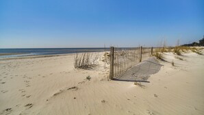 A sandy beach with footprints leading to a striped gate, overlooking the ocean. - Gulfport Oceanfront Vacation Rental: Walk to Beach (Gulfport)