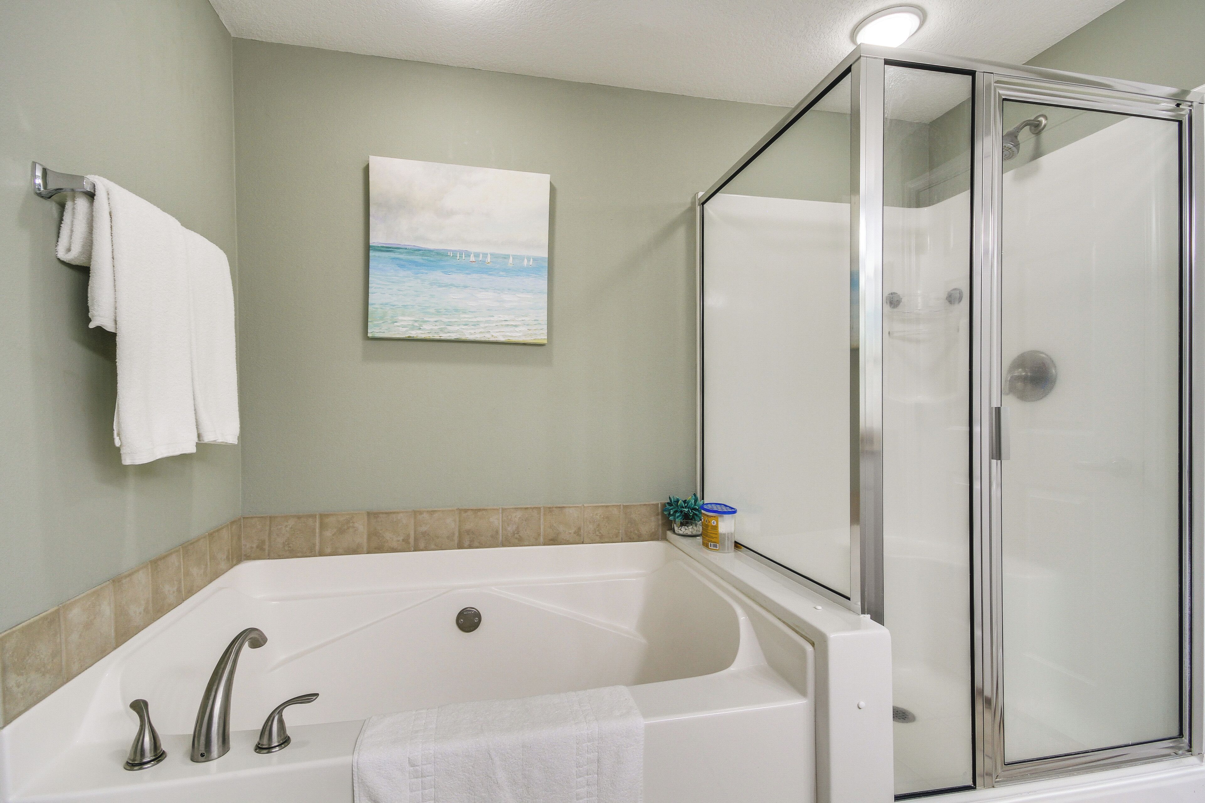 Un bagno con vasca, doccia vetrata e un quadro raffigurante una spiaggia.