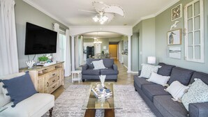 A spacious living room with a large flat-screen TV, a ceiling fan, and a coffee table with decorative items. - Gulfport Oceanfront Vacation Rental: Walk to Beach (Gulfport)