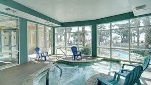 An indoor swimming pool with clear glass walls, blue chairs, and a view of palm trees and a poolside area. - Gulfport Oceanfront Vacation Rental: Walk to Beach (Gulfport)