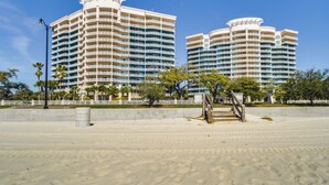 A beachfront hotel with multiple balconies, a sandy beach in the foreground, and palm trees. - Gulfport Oceanfront Vacation Rental: Walk to Beach (Gulfport)